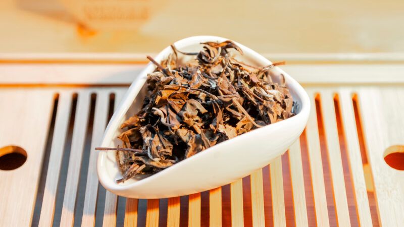 on a wooden tray is a white ceramic container with loose Shou Mei tea