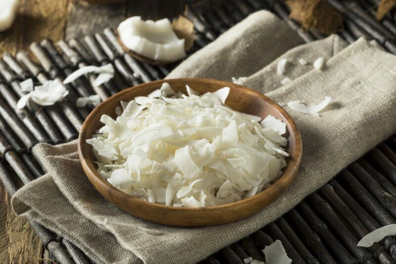 A brown bowl filled with shredded coconut, on a napkin of some type