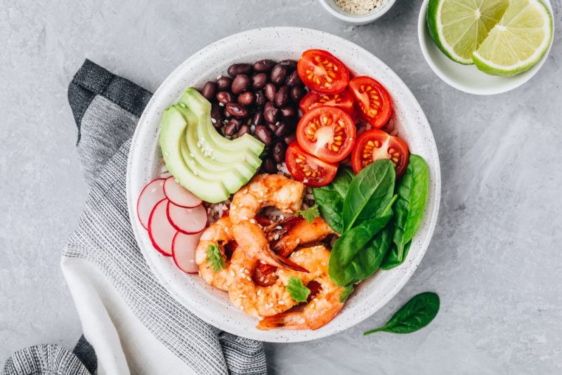 A white bowl with shirmp and a selection of burrito ingredients