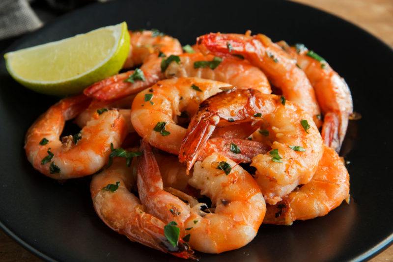 A black plate that contains cooked shrimp and a lime wedge