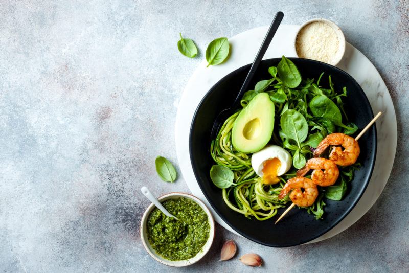 A black bowl with keto ingredients and pesto on the side