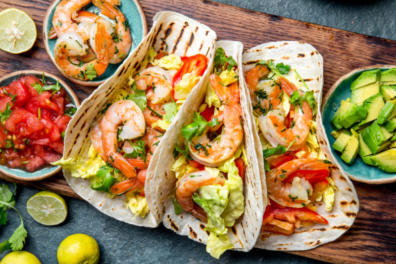 Three shrimp tacos with various bowls of fillings on the table