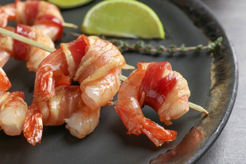 A black plate with lime wedges, shrimp, and bacon