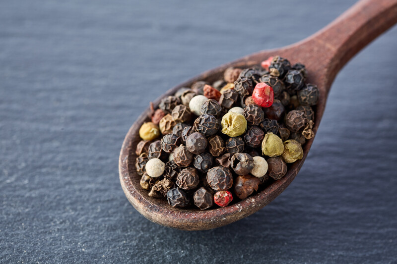 Wooden ladle full of whole Sichuan peppers resting on a black marble surface.