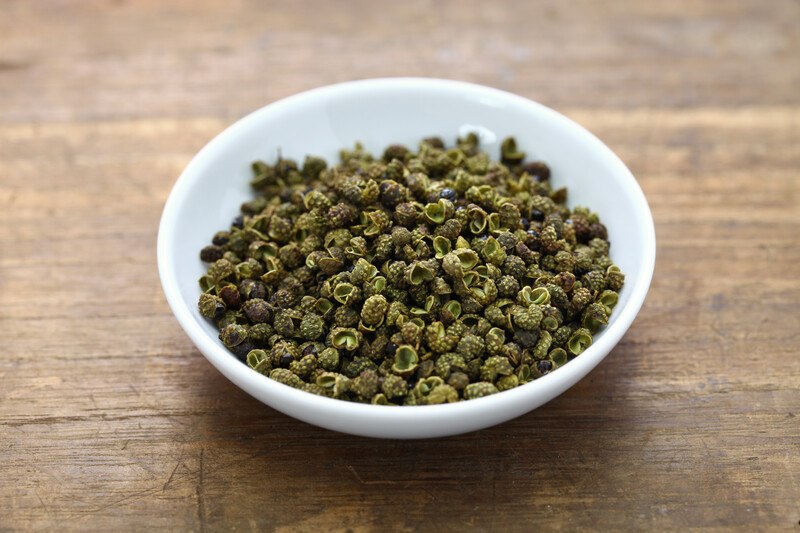 a wooden surface with a white shallow bowl with Sichuan peppercorns