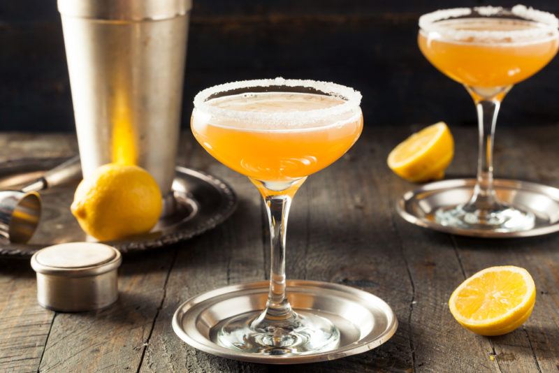 Two sidecar cocktails on a table with a cocktail shaker