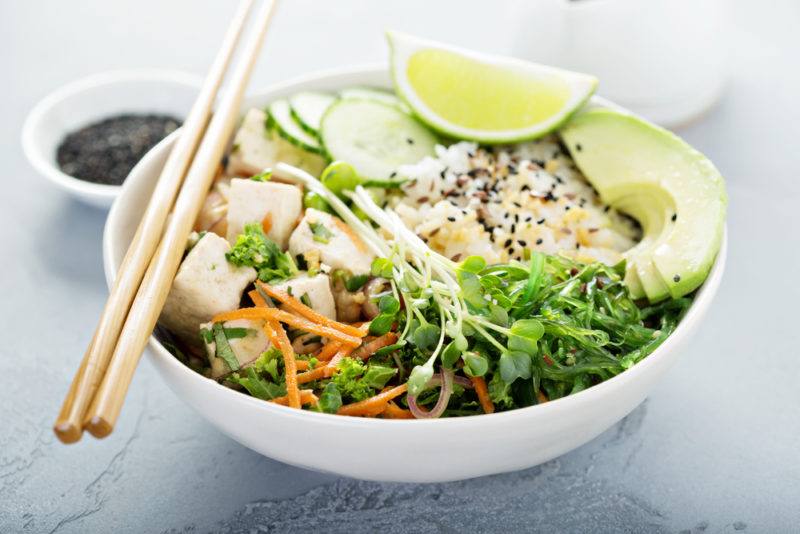 A white bowl that contains tofu, greens, and rice