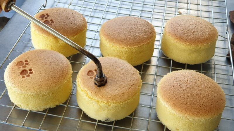 A wire cooling tray with six Chinese egg cakes that are being stamped with small paw prints