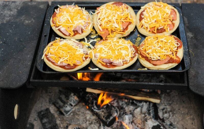 A pan on a campfire that is being used to make six campfire pizzas