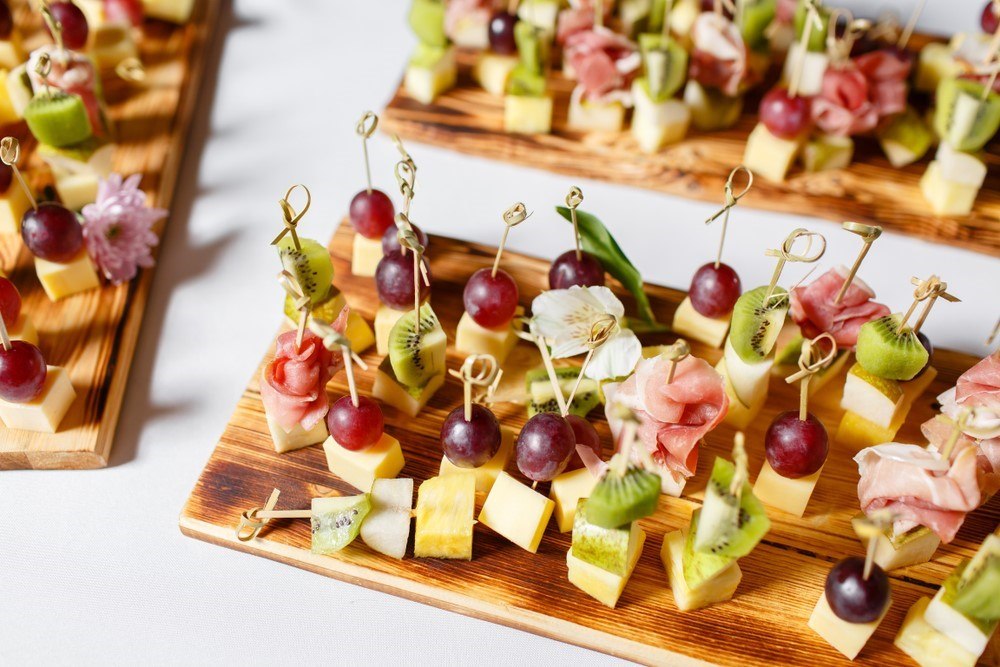 Three wooden planks with cheese, meat, and fruit on skewers