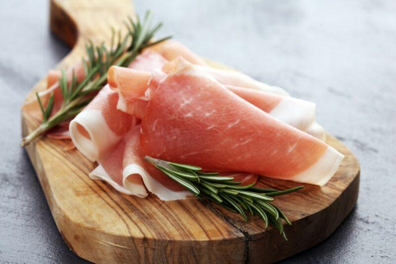 A wooden board with slices of cured ham and some rosemary