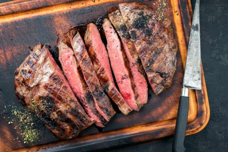 A large wooden board with sliced flank steak next to a knife