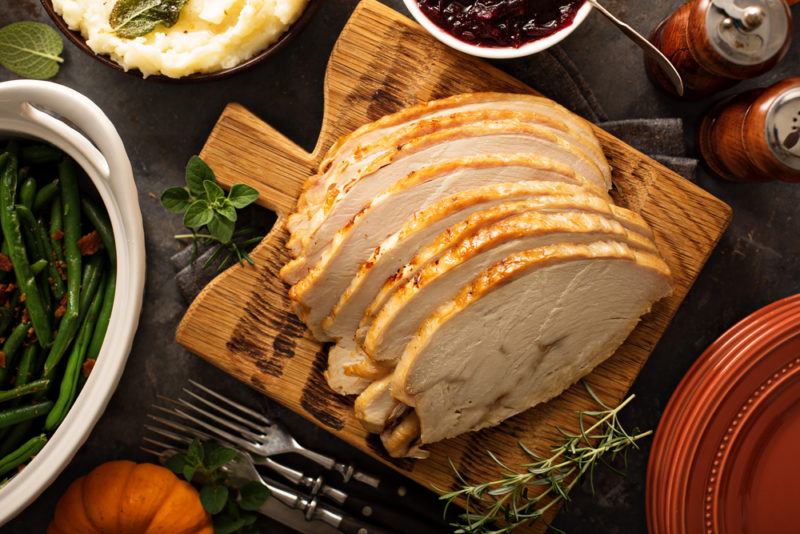 Sliced roast turkey on a wooden board, surrounded by various Thanksgiving sides