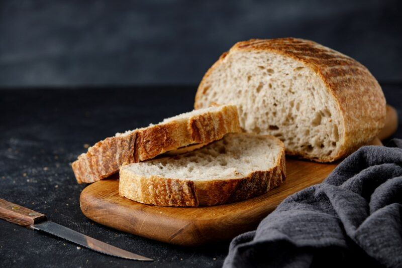 A wooden tray with two slices of sourdough, with a sourdough loaf