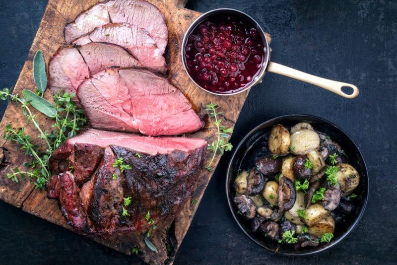 A wooden board that has a piece of venison with sone slices cut from it, along with a condiment and mushrooms