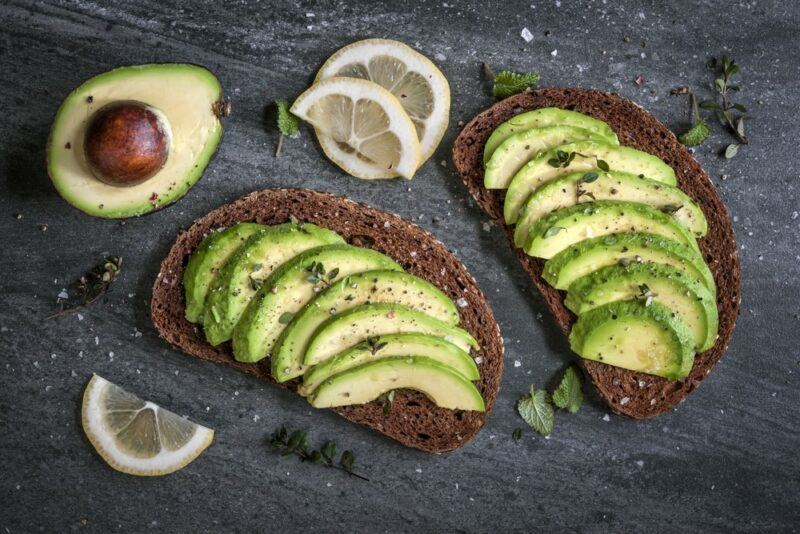 Two pieces of rye toast with sliced avocado next to half an avocado