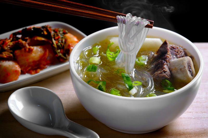 bowl of korean noodle soup with beef bone and kimchi as a side