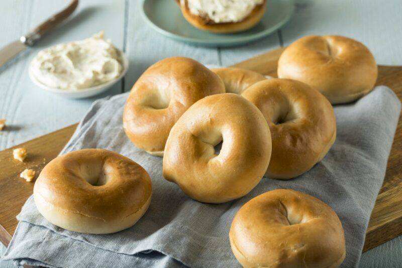 A selection of small bagels next to some cream cheese on a light blue or green table