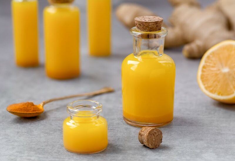 A few small bottles of turmeric shots, with a spoon of turmeric powder and half an orange