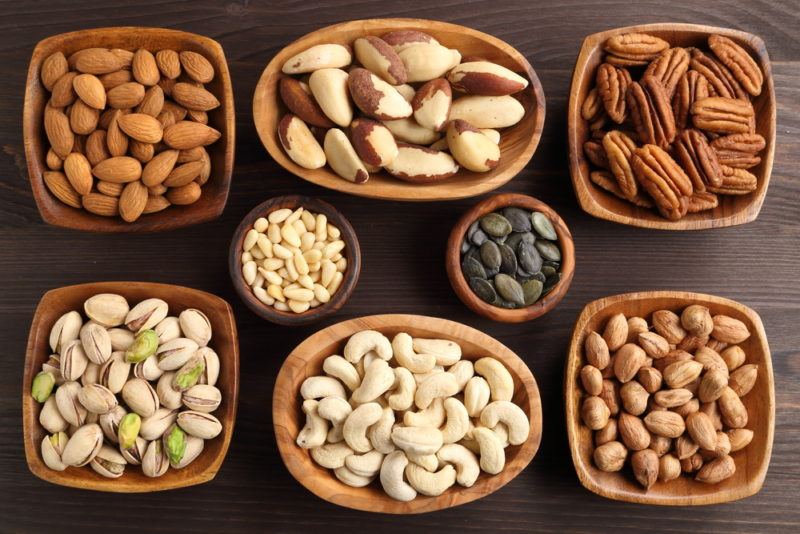 Various small bowls that each contain a different type of nut or seed, including almonds, brazil nuts, and cashews