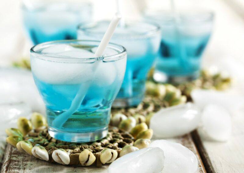 Small glasses of a blue lightning cocktail with ice and a straw