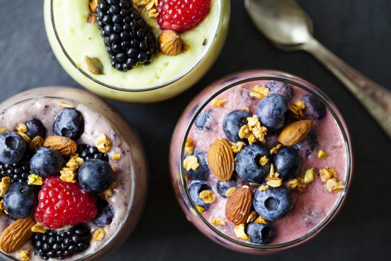 Three glasses containing smoothies with fruit and nuts as toppings