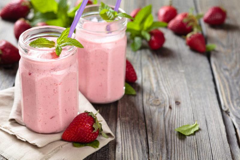 Two strawberry smoothies on a table with fresh strawberries