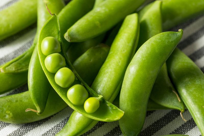 Various snap pea pods on a table with one open showing the contents