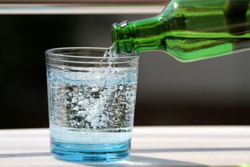 Soda water being poured into a glass from a green bottle