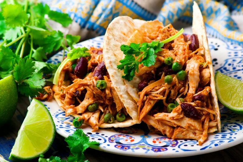 A plate with two soft tacos that have been made with shredded chicken and beans