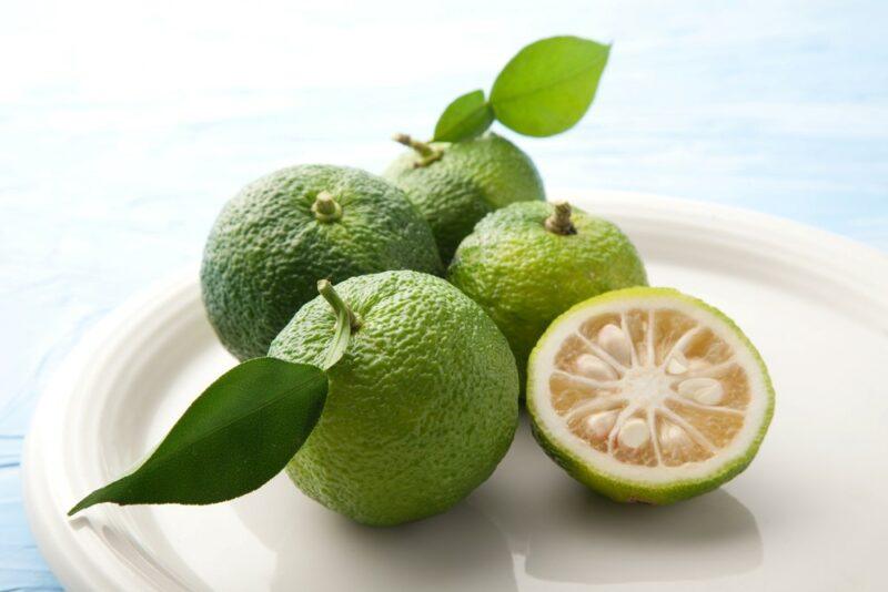 A white plate containing four whole green yuzu fruits, plus one half