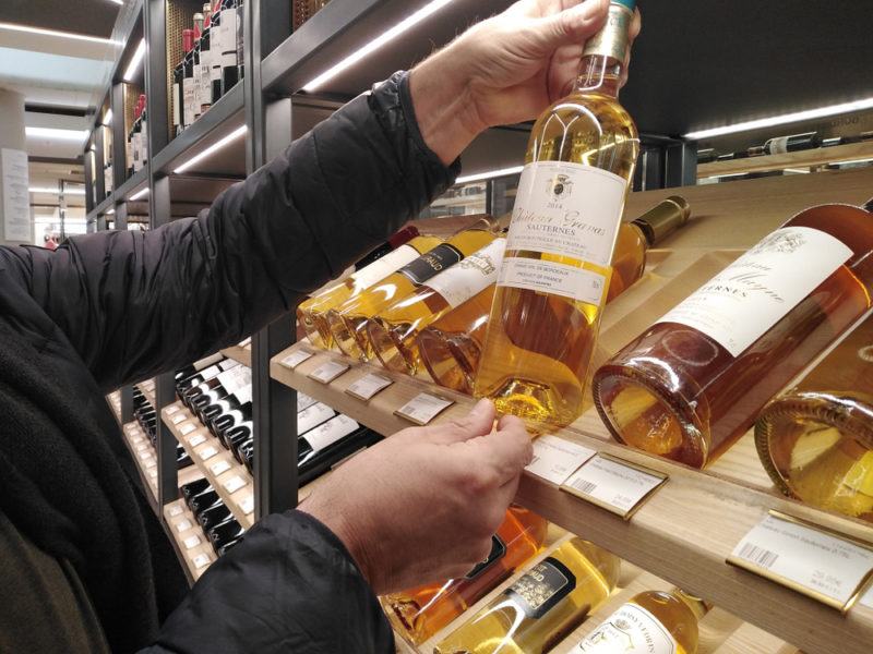 Someone choosing a bottle of sauternes from the shelf that contains many different bottles of the wine