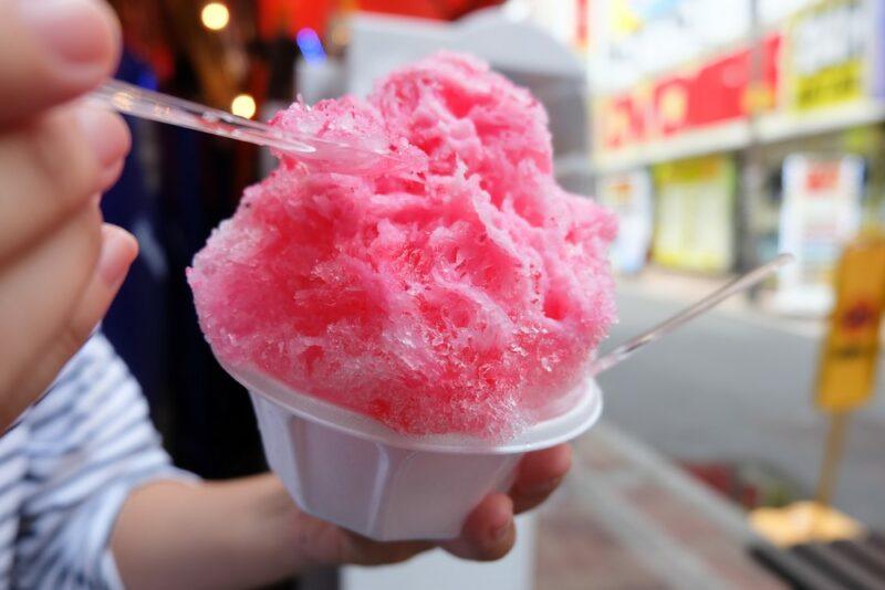 Someone with a large red strawberry daiquiri snow cone, eating it with a spoon