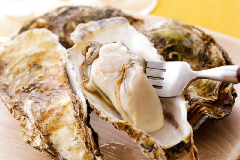 Oysters on a plate with some type of sauce, where someone is using a fork to grab some of the flesh