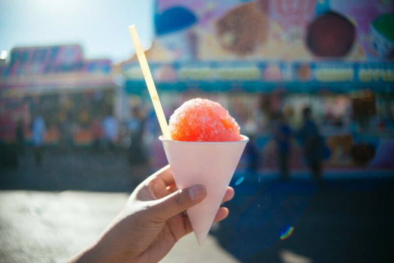 Someone holding a paper cone with a cherry cheesecake flavored snow cone