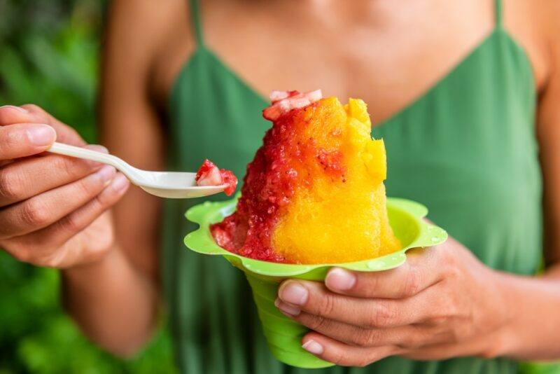 A woman with a green top holding a green container with a spicy mango snow cone and a spoon