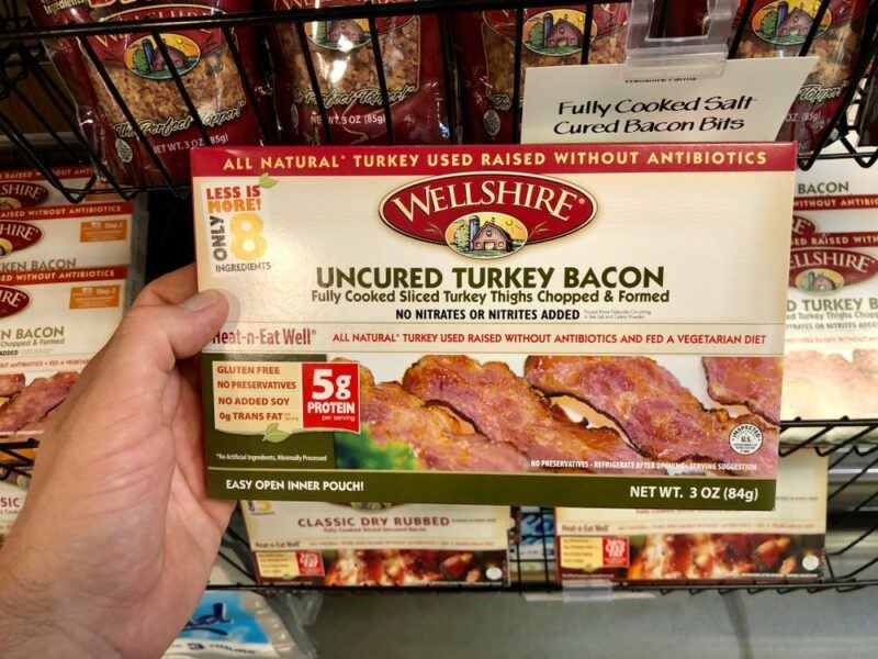 Someone holding up a box of uncured turkey bacon in a grocery store