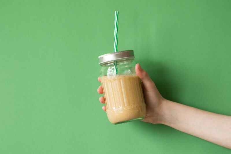 Someone holding up a shake in a mason jar against a light green background