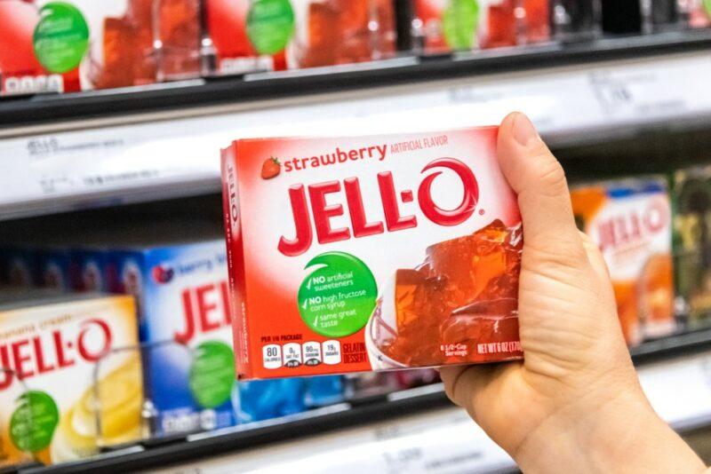 Someone holding a package of red jello in a grocery store, with other boxes visible on the shelves