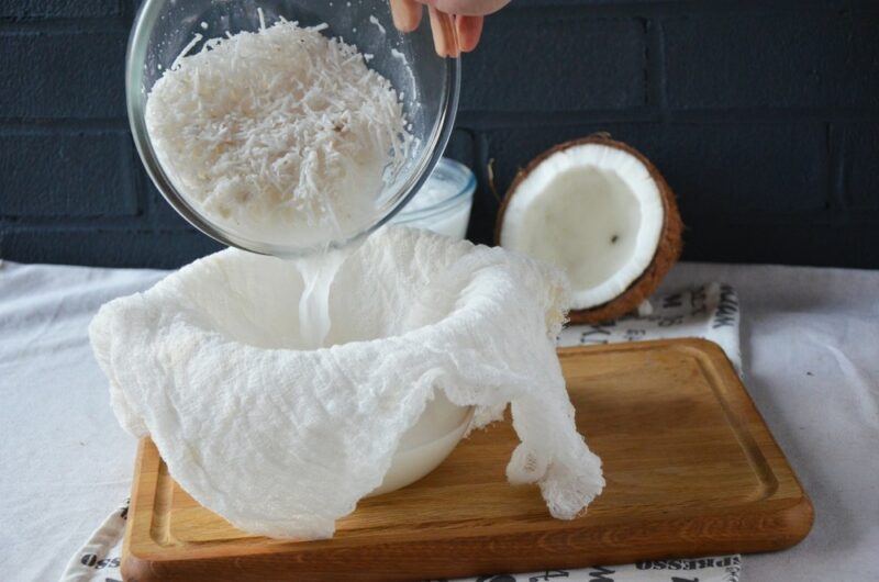 Coconut milk being made at home, where the liquid is being poured off the shredded coconut and into a cheesecloth