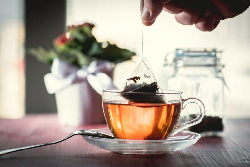 A mug of tea on a table, where someone is dunking the teabag, there is a pot plant in the background