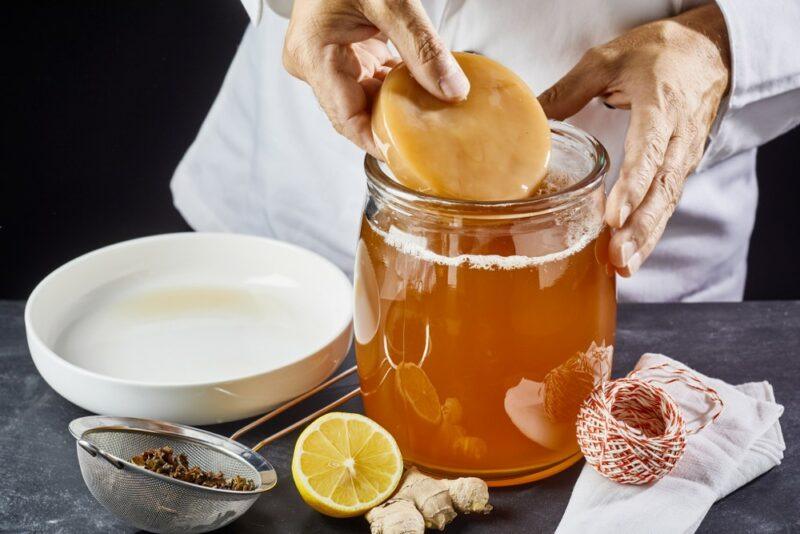 Someone in a kitchen preparing kombucha, with the SCOBY in their hand