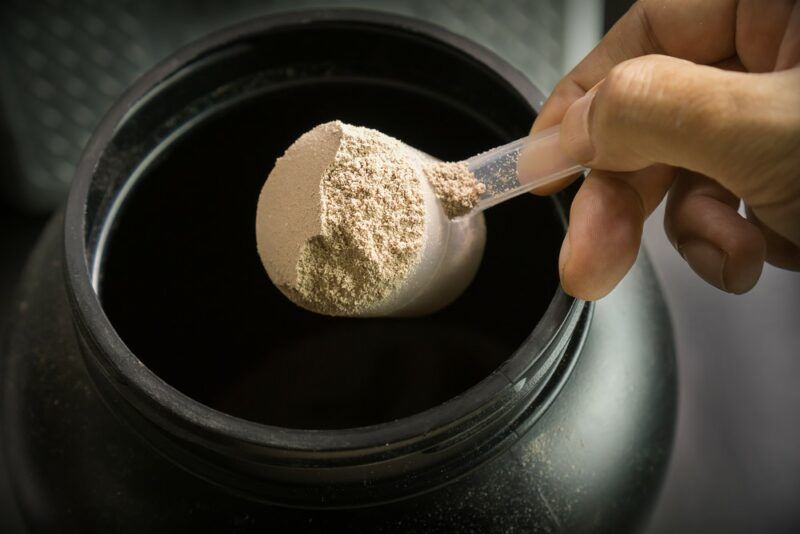 Someone scooping out creatine powder from a large black jar