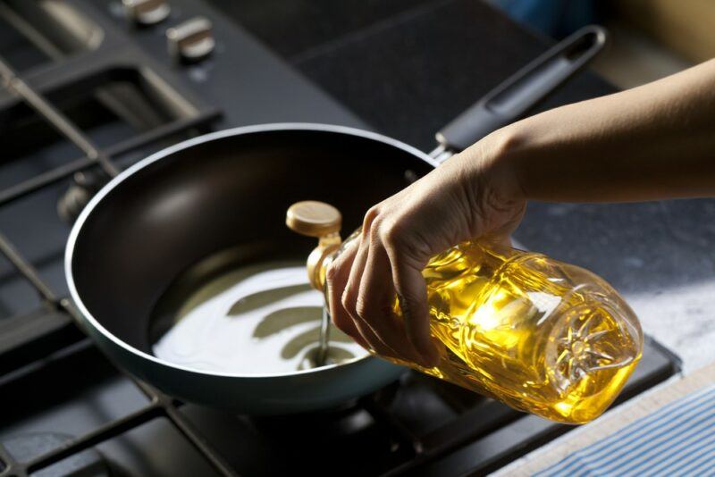 Someone pouring vegetable oil into a fry pan as they are cooking