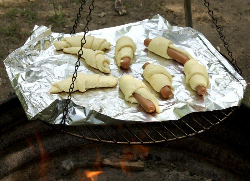 A frame with tinfoil over a fire being used to cook pigs in a blanket