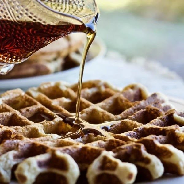 A large sourdough waffle on a plate with syrup being poured onto it