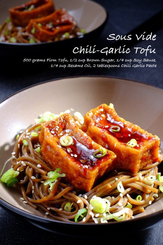 Two black and white bowls containing noodles with spring onions and sesame seeds, each topped with two pieces of chili-garlic tofu