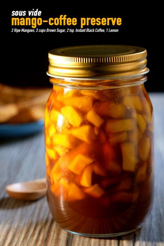 A jar containing sous vide mango coffee preserve on a table, next to a spoon with a dessert in the background