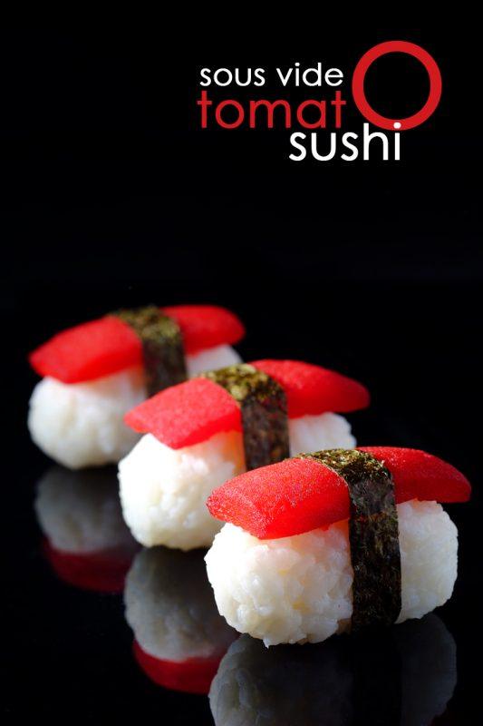 Three pieces of sushi made using rice, seaweed, and tomato, against a black background. Their reflection can be seen on the black table.