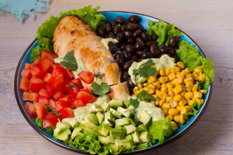 A blue bowl with sliced chicken, peppers, corn, and other ingredients